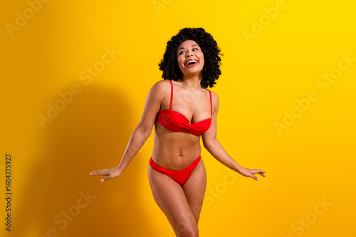 Joyful woman in red bikini radiating happiness against yellow background, embracing summer vibes and celebrating beauty