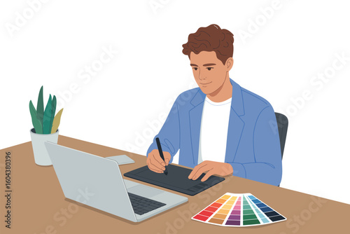 A man using a graphic tablet and a laptop at a desk with a color palette and a plant on the side