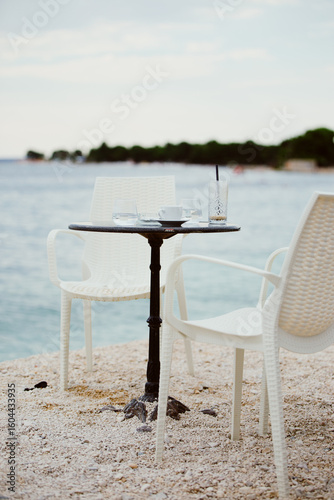 Table with chairs and empty glass and coffee cup on the seashore. Beach bar