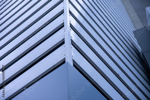Detailed view of a sharp corner of a building with sleek horizontal metal slats and reflective surfaces in cool blue tones.