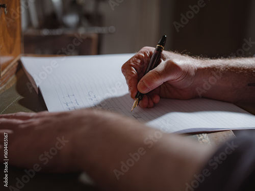 A person's hand holding a pen and writing on a lined notebook