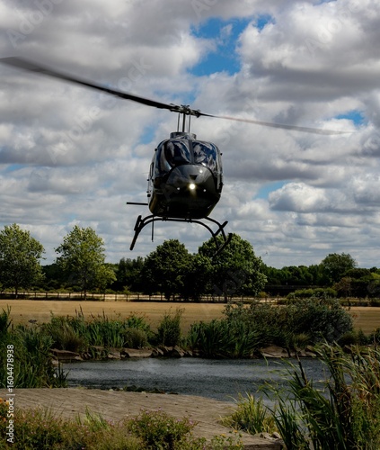 Helicopter hovering over scenic pond.