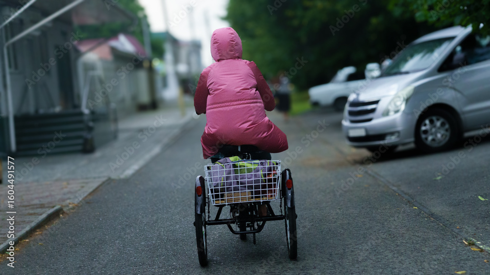 Obraz premium Person in pink raincoat riding a tricycle down a quiet street on a rainy day