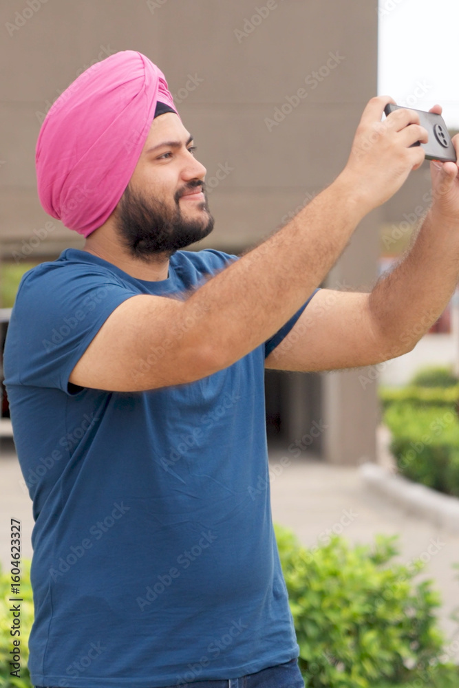Naklejka premium Vertical Photo of Sikh Indian Man Clicking Pictures with Phone
