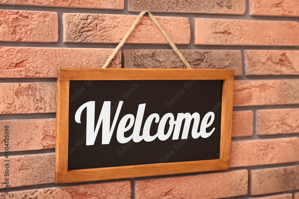 Obraz premium Small chalkboard with word Welcome hanging on brick wall