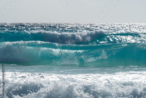 Fototapeta Naklejka Na Ścianę i Meble -  Turquoise ocean waves rolling and crashing against the shore on a bright, sunny day, creating a vibrant seascape filled with energy