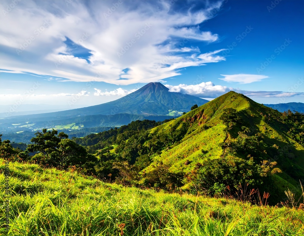 Fototapeta premium Lush green hills meet a volcanic peak under a vibrant sky