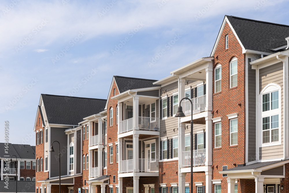 Fototapeta premium Detail of a row of brick and tan vinyl siding townhomes with white posts on the patios and a blue sky.