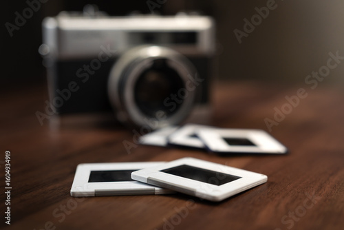 Several photo slides resting on a wooden table, accompanied by a vintage camera in the background, evoke nostalgic memories of past travels and cherished experiences