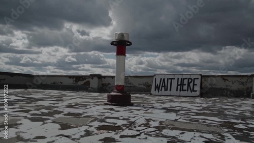 Dark clouds blanket rooftop with a solitary pole and sign urging to wait as storm approaches