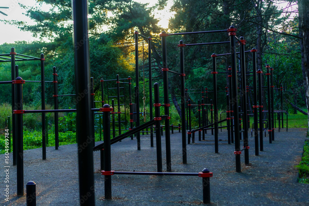 Fototapeta premium Outdoor fitness area featuring exercise equipment surrounded by trees during sunset in a quiet park