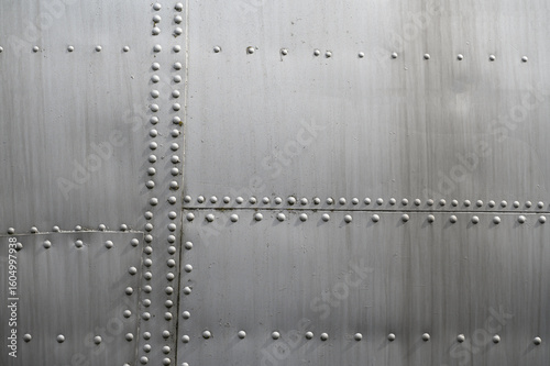 Close-up of metal surface of aircraft fuselage, silver in color, with many rivets mounted in it. Background, aircraft texture