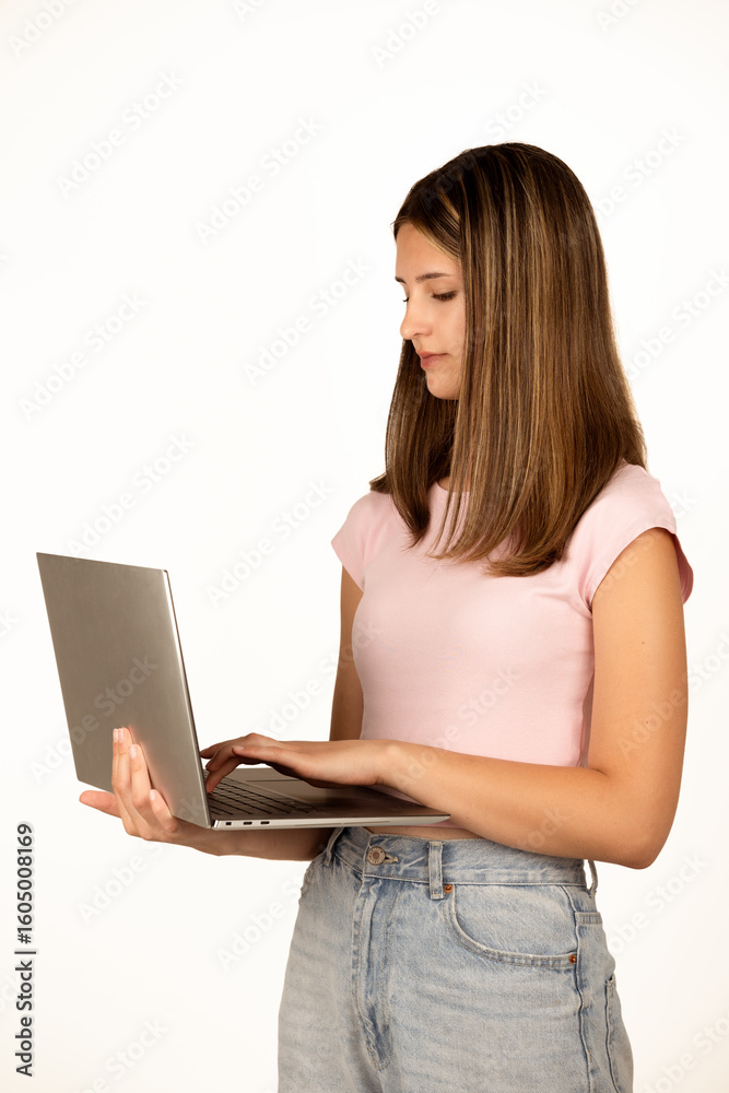 Teenage girl with straight brown hair wearing a pink t-shirt and jeans holds and types on a laptop, isolated on a white background. Suitable for concepts related to technology, remote work, online