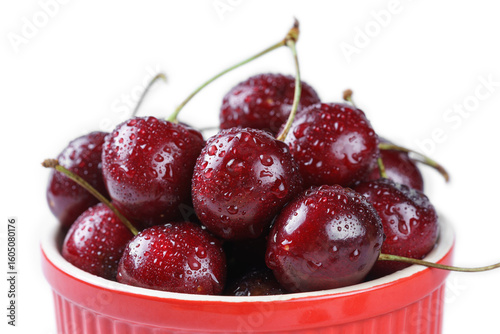 Close up, macro of organic fresh sweet cherries with water drops in red bowl isolated on white background. Seasonal fruit, nutrition, summer snack, healthy food and eating visual.