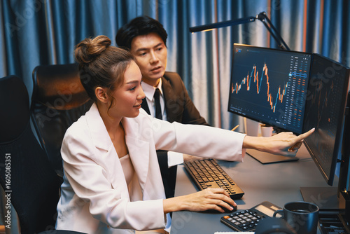 Obraz na plátně Smiling Asian business traders pointing to dynamic stock exchange data screen profit value online website program at night time at home office