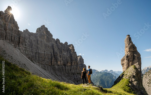 Iconic friulan mountain Campanile Di Val Montanaia, Dolomiti Friulane, Val Cimoliana, Cimolais Friuli Venezia Giulia, Italy. Two hikers stand on a grassy ledge, admiring the dramatic mountain scenery.