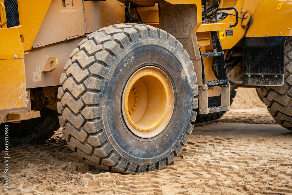 Heavy construction machinery tire on sandy ground at worksite showing rugged tread used in earthmoving operations and infrastructure construction environments Heavy construction machinery tire on sandy ground at worksite showing rugged tread used in earthmoving operations and infrastructure construction environments