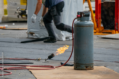 Obraz na płótnie Propane gas cylinder with torch flame at roofing construction site with worker i