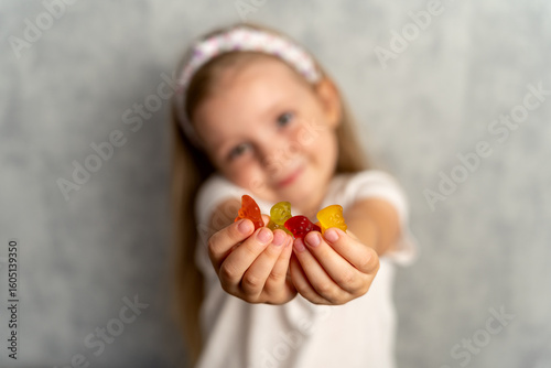 Vitamins for  kid. Little happy girl holding vitamins in the form of jelly bears. Soft focus on the face. Multivitamins in jelly.