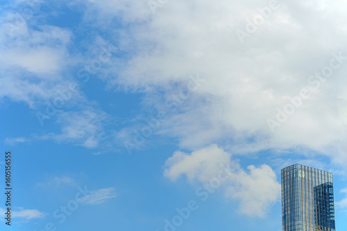  A modern tall building with mirrored glass reflects the cloudy sky, evoking a sense of harmony between architecture and nature. Its elegant silhouette rises above the urban landscape.
