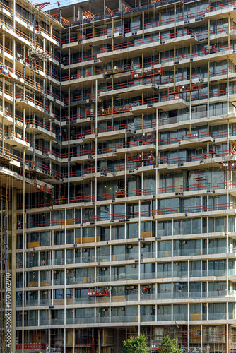 A multi-story building with balconies is under active construction, surrounded by scaffolding and equipment. The architectural structure showcases the scale of the project and urban development.