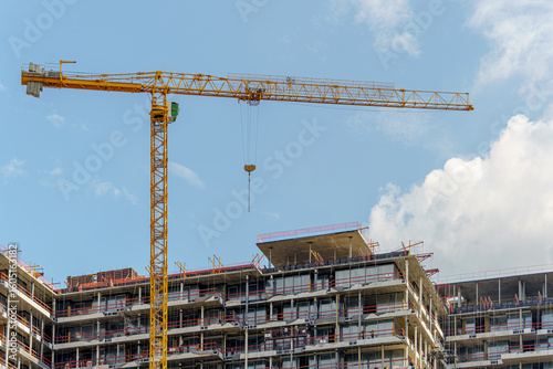 Slika na platnu Construction of a multi-unit residential building is underway with the help of a tower crane against a backdrop of blue sky and clouds