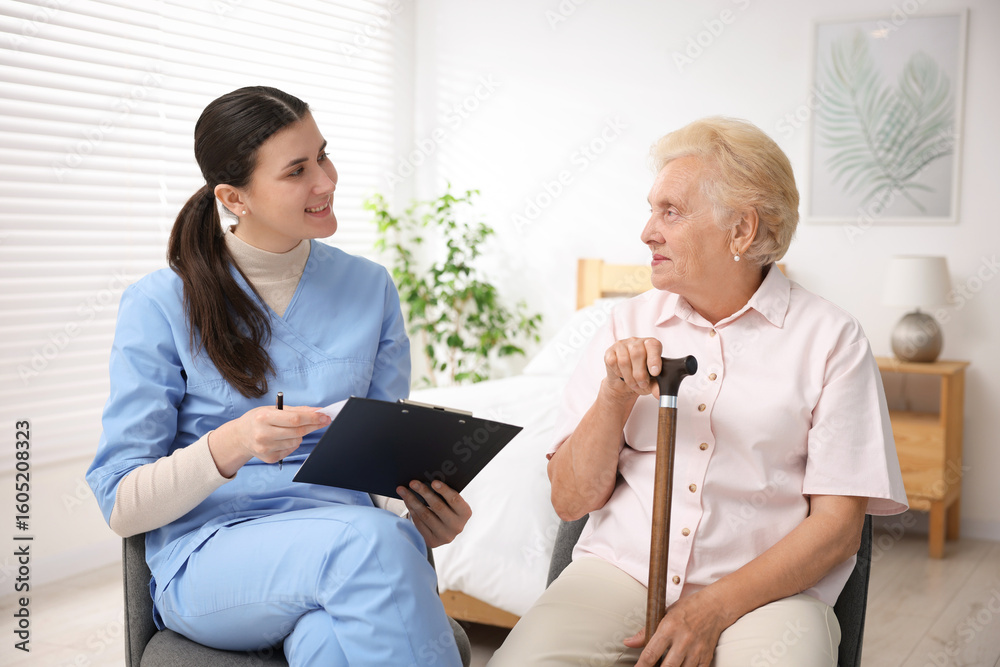 Obraz premium Nurse with clipboard examining senior woman indoors. Home health care service
