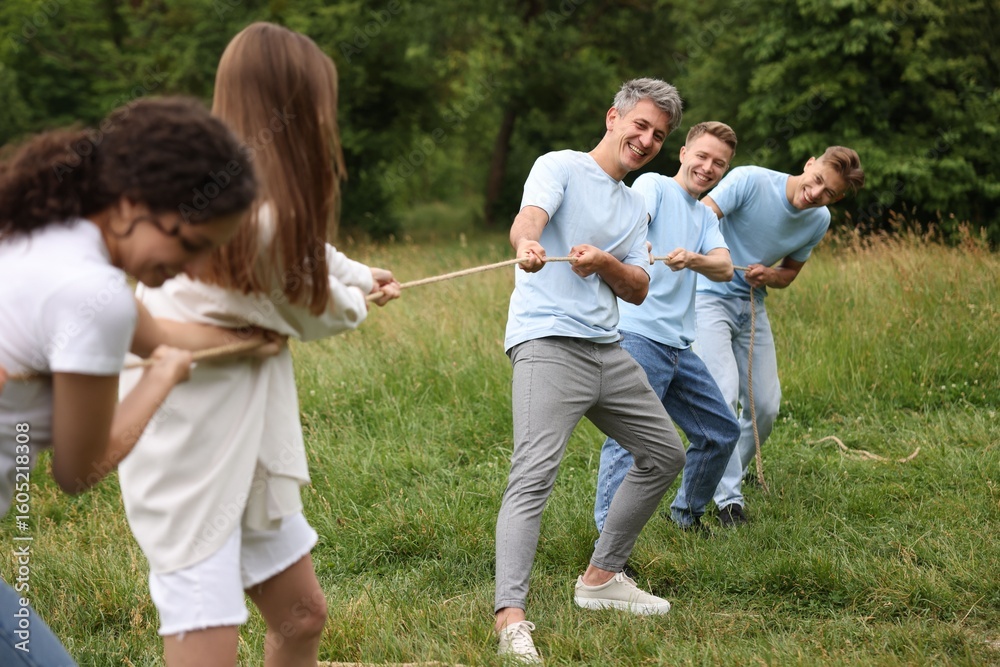 Fototapeta premium Team building. Group of happy people playing tug of war with rope outdoors