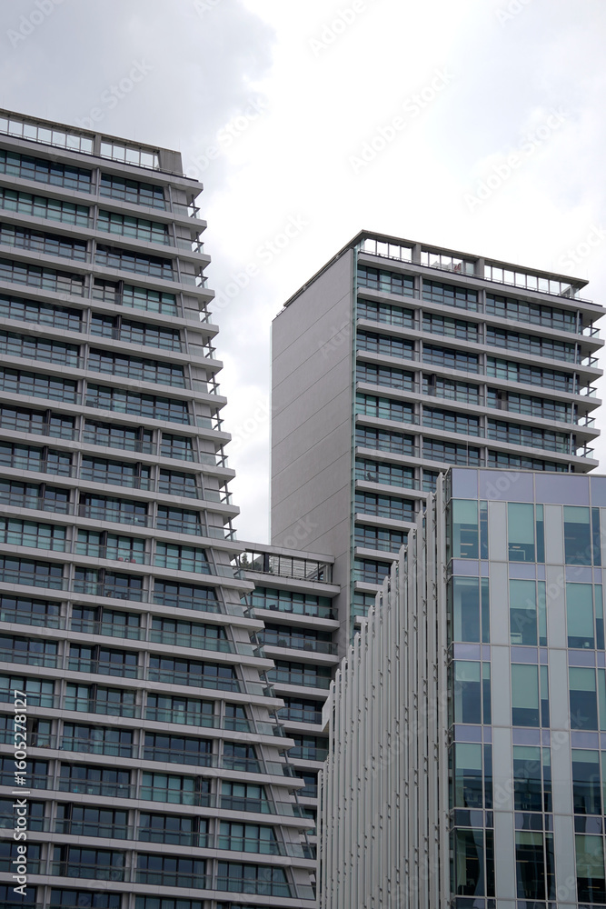 Fototapeta premium Two modern high-rise residential towers with sloped facades and glass balconies. Contemporary architecture dominates the skyline, blending symmetry and urban lifestyle design.