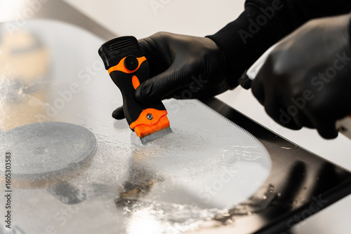 Foto Technician uses scraper to clean the surface of a new windshield post-replacement