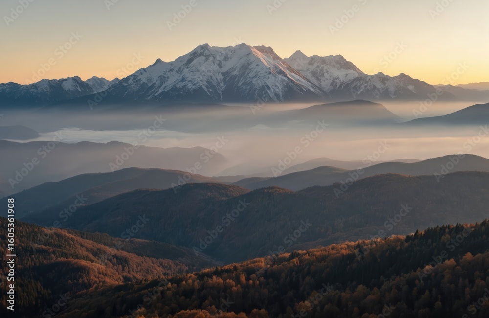 Fototapeta premium Majestic mountain range with snow-capped peaks at sunset. Layers of mist and hills create depth in this landscape. Warm golden light illuminates the scene, perfect for travel and nature themes.