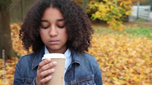 Beautiful mixed race African American girl teenager young woman wearing a blue denim jacket outside sad or depressed then happy smiling drinking coffee or tea