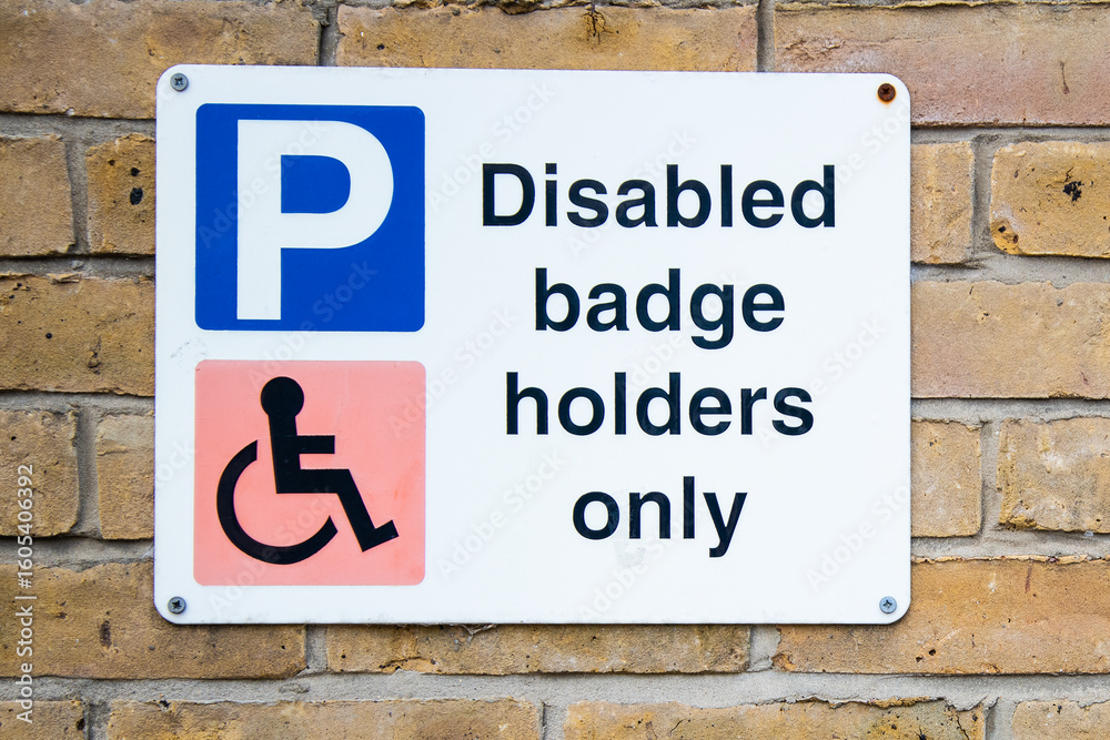 Disabled badge holders only parking sign mounted on a brick wall, indicating restricted parking for blue badge holders in a designated area. Disabled badge holders only parking sign mounted on a brick wall, indicating restricted parking for blue badge holders in a designated area.