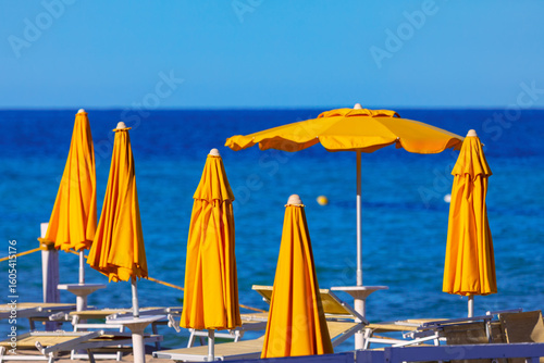 Bright yellow beach umbrellas stand over the tranquil blue sea. Beach umbrellas stand guard over the tranquil blue sea