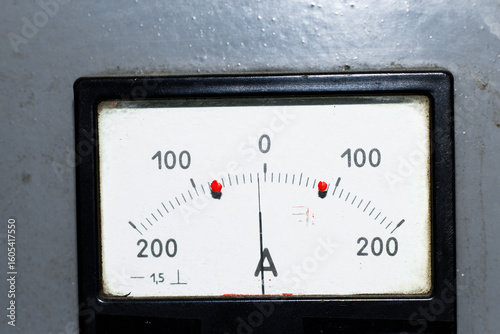 Close-up of an analog ammeter with needle at zero and red limit markers. Industrial gauge for measuring electric current, retro-style equipment