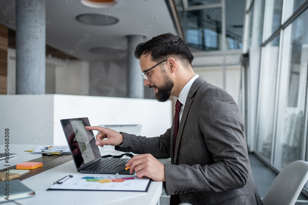 Fototapeta premium Businessman analyzing charts on laptop in modern office