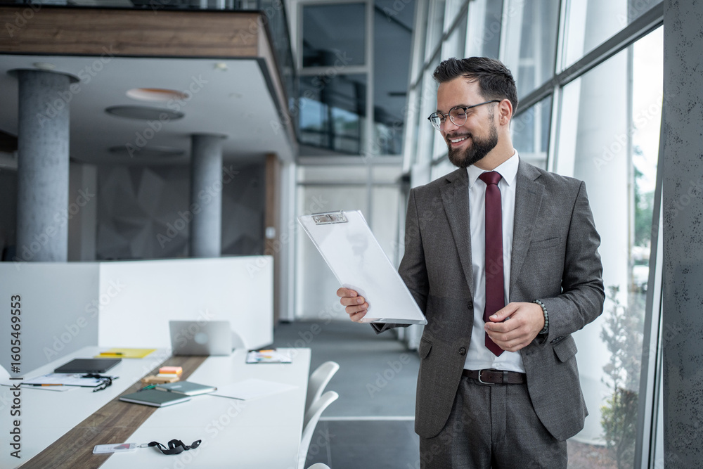 Fototapeta premium Smiling businessman reading documents in modern office
