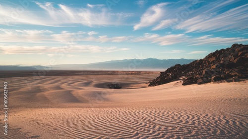Tranquil desert landscape featuring sand dunes, rocky outcrop, and distant mountains