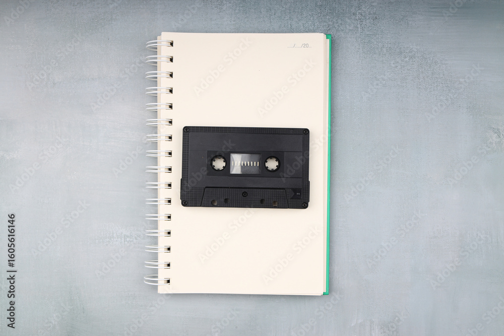Obraz premium Retro audio cassette tape from the 80s and 90s on a white background. blank playlist on notebook. Top view, nostalgic concept.
