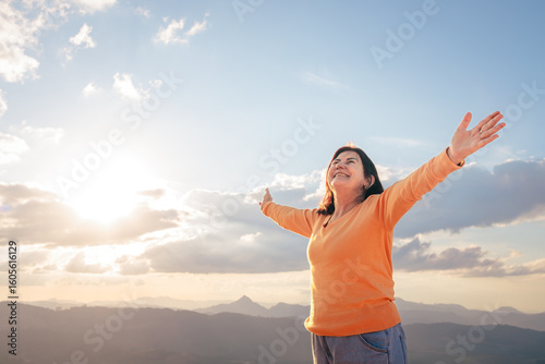 Mature Brazilian woman feeling joyful and free with arms wide open, enjoying a sunny day in the mountains. A moment of gratitude and connection with nature.