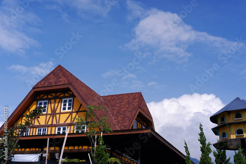 Wallpaper Mural The roof of the house is a combination of trapezoid and triangle with brown tiles, the building has yellow walls with white window frames. The building is against a backdrop of a bright blue sky. Torontodigital.ca