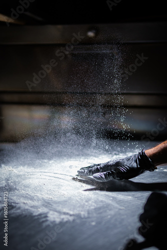Chef spreading flour on stainless steel counter for pizza preparation