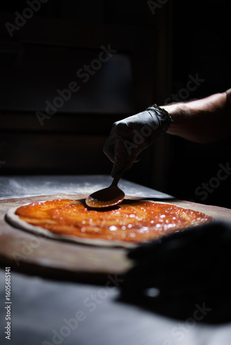 Chef spreading tomato sauce on pizza dough in restaurant kitchen