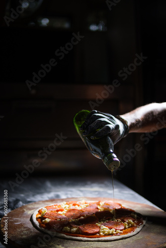 Chef pouring olive oil on delicious pepperoni pizza
