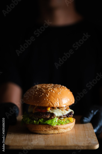 Chef showing delicious hamburger on wooden board
