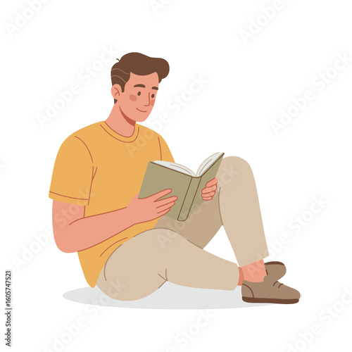 A young man sits cross-legged on the floor, absorbed in reading a book with a focused and relaxed expression.