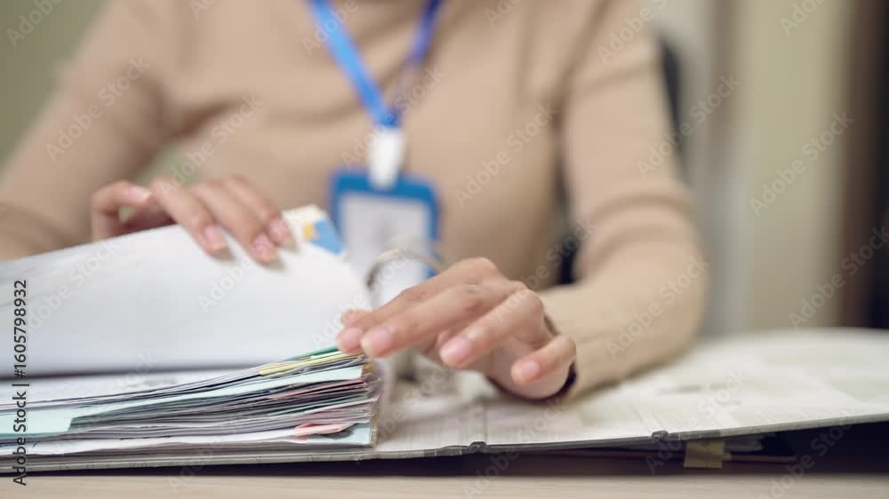 A woman is looking at a stack of papers. She is holding a piece of paper in her hand A woman is looking at a stack of papers. She is holding a piece of paper in her hand