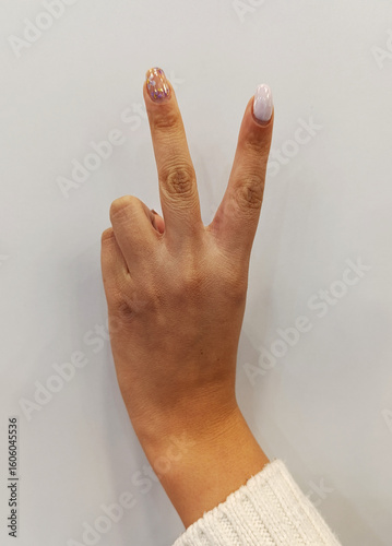 Female hand with manicure showing the victory gesture on a white background, symbol of peace or triumph.