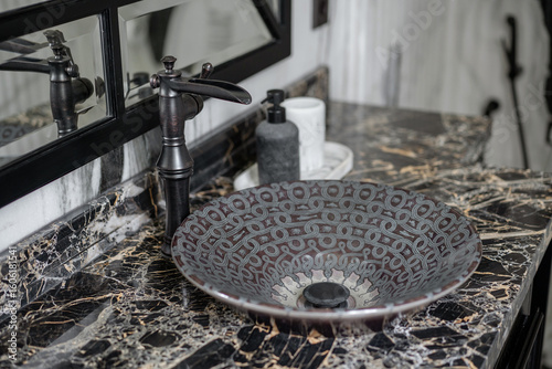 Bilde på lerret An elegant bathroom setup with a unique patterned vessel washbasin on a black marble top, complemented by a vintage-style dark bronze waterfall faucet
