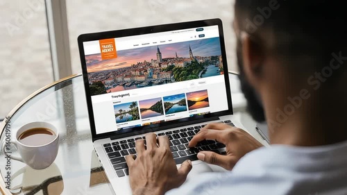 African American man plans vacation on laptop with travel agency website shown
